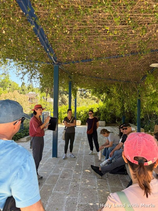 Maria Lando guiding a group under a vine pergola in Ein Karem