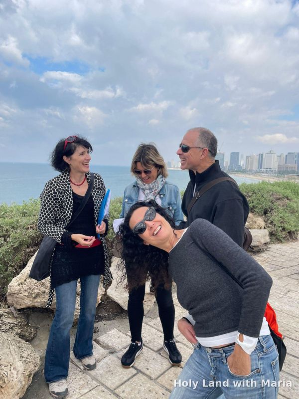 Maria Lando laughing with guests at a Jaffa viewpoint over the sea