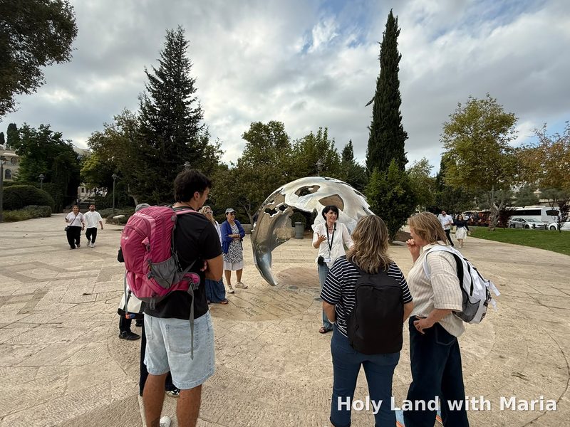 Maria Lando guiding a group of tourists in Teddy Park, Jerusalem, beside Heinrich Bünting's map of the world