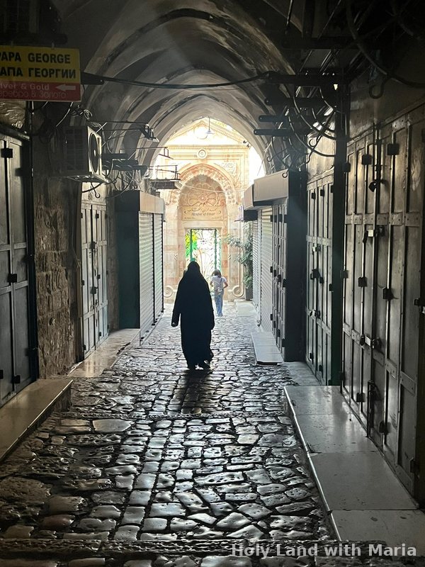A woman walking down a vaulted market lane towards the Mosque of Omar in the Old City of Jerusalem