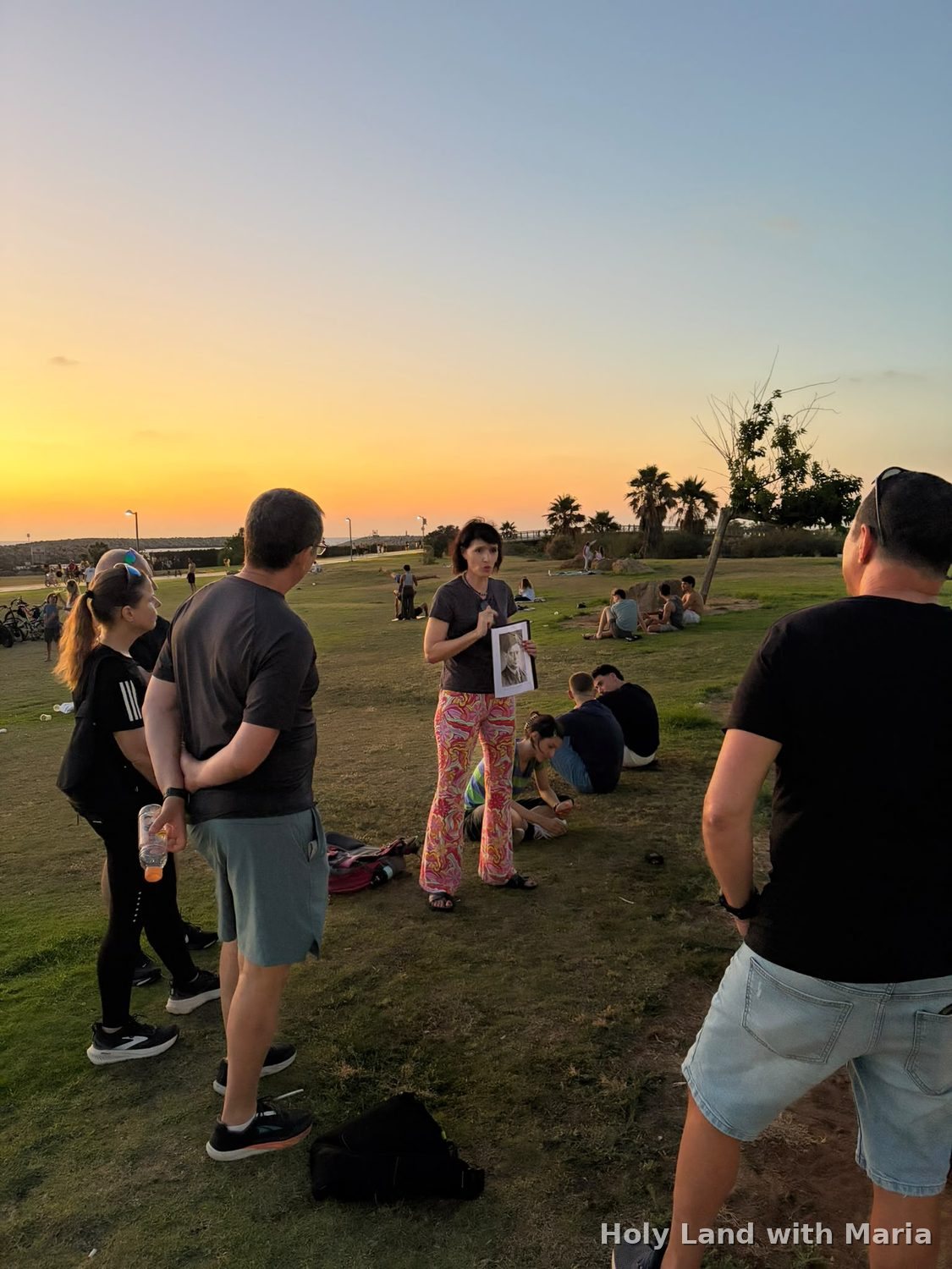 Maria Lando telling the story of the Maccabiah with a historical photograph, on a Tel Aviv tour at sunset